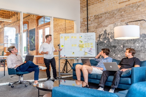 Three men in a meeting using laptops and a whiteboard