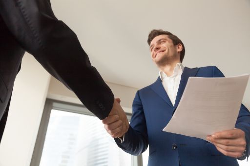 Smiling man holding a sheet of paper while shaking hands with someone else